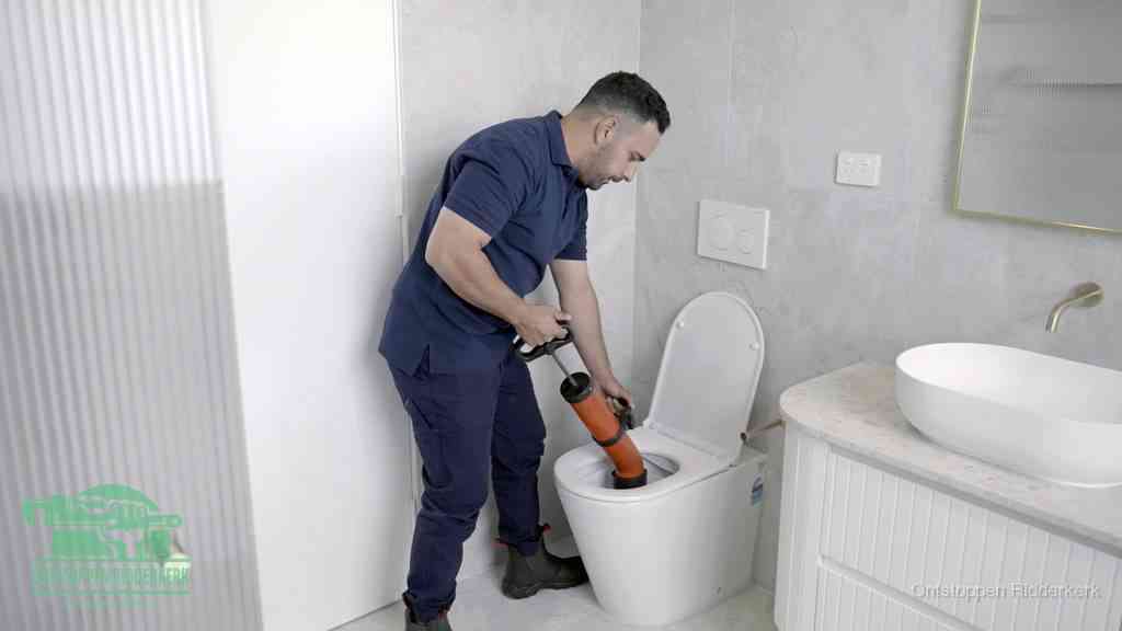 Een monteur buigt over een wandcloset en duwt met de hand een persluchtontstopper in de toiletpot om de verstopping handmatig los te maken in Ridderkerk