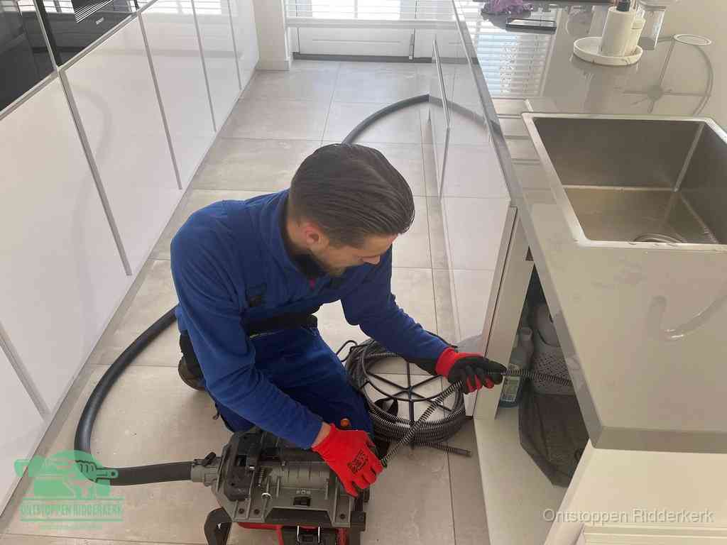 Een monteur ontstopt de keukenafvoer onder de spoelbak met een elektrische veermachine in Ridderkerk