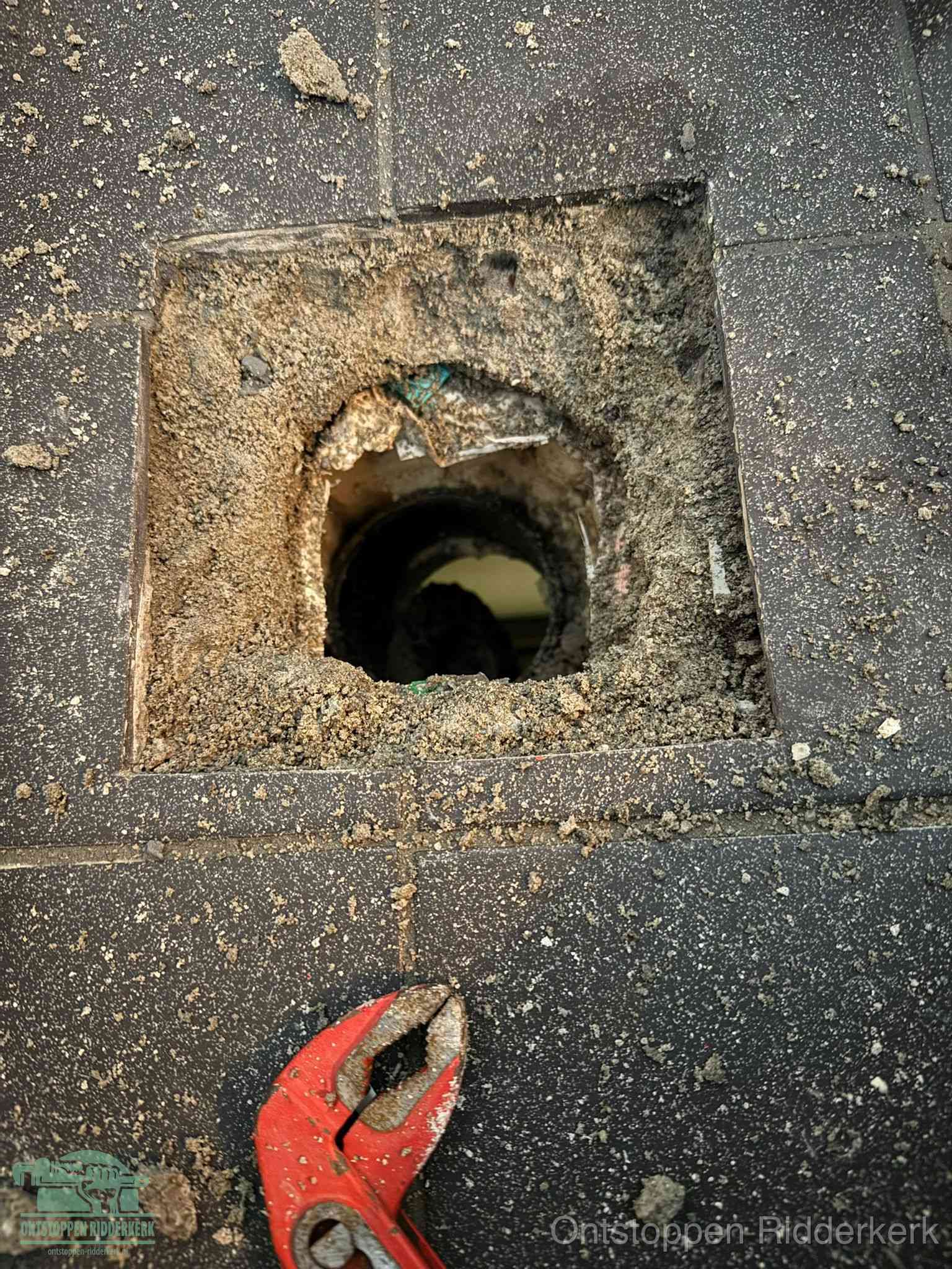Een geopend rioolputje in een betontegelvloer met losgemaakt rooster en een zichtbare ronde afvoerbuis, het achterhalen waar de afvoerverstopping zit in Ridderkerk