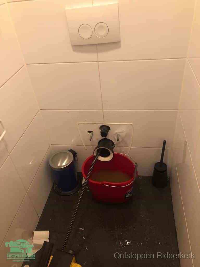 Een ontstopte wand-wc met verwijderde toiletpot waar een ontstoppingsveer in de wanduitgang verdwijnt, het achterhalen waar de verstopping zit in Ridderkerk