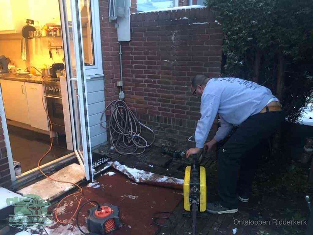 Een monteur werkt buiten bij een open riool-/grondput met een elektrische ontstoppingsmachine om een verborgen afvoerprobleem op te sporen in Ridderkerk