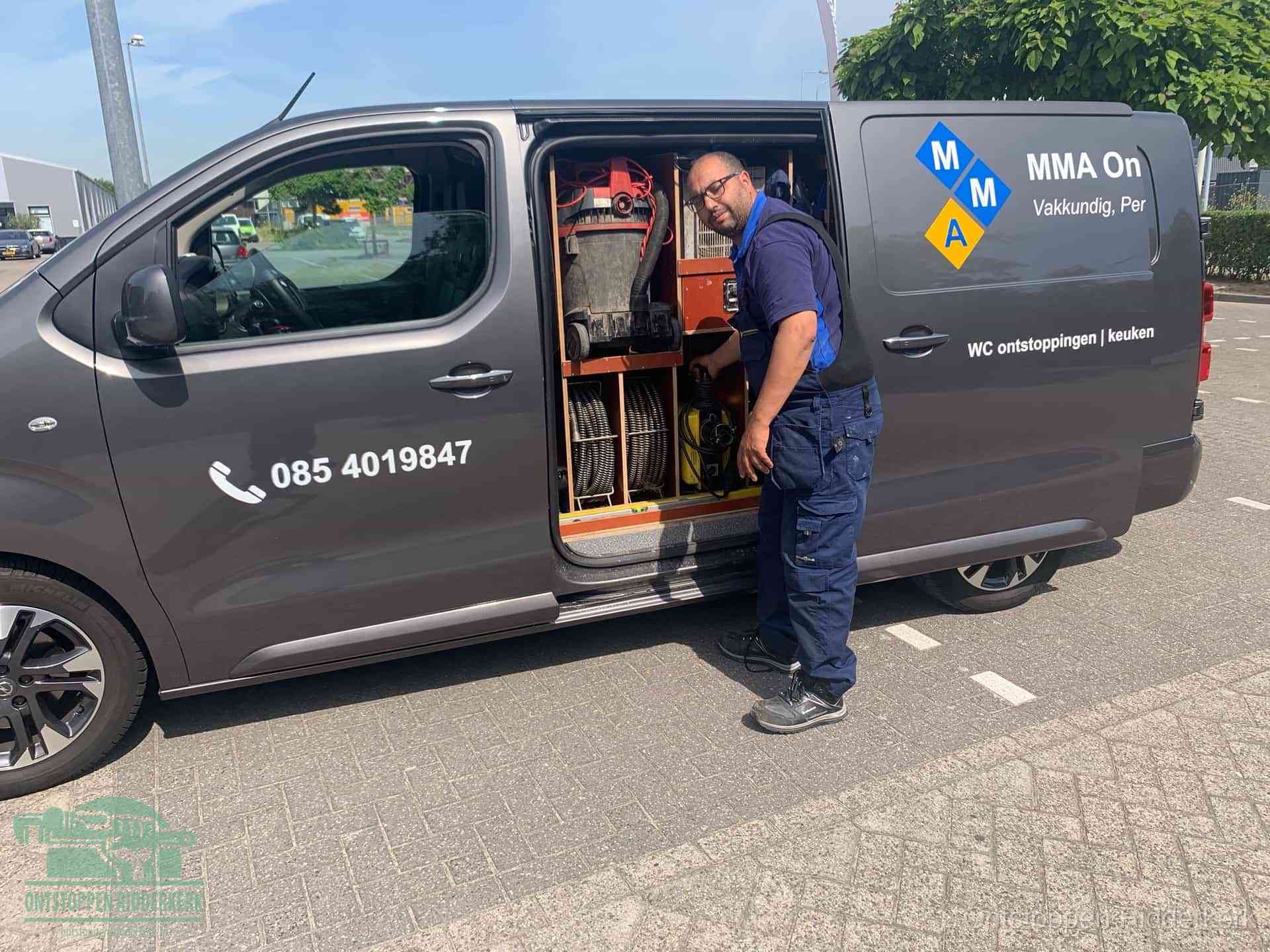 Een monteur bij de open schuifdeur van zijn bedrijfsbus op een parkeerplaats, klaar om de oorzaak van terugkerende afvoerverstoppingen aan te pakken in Ridderkerk