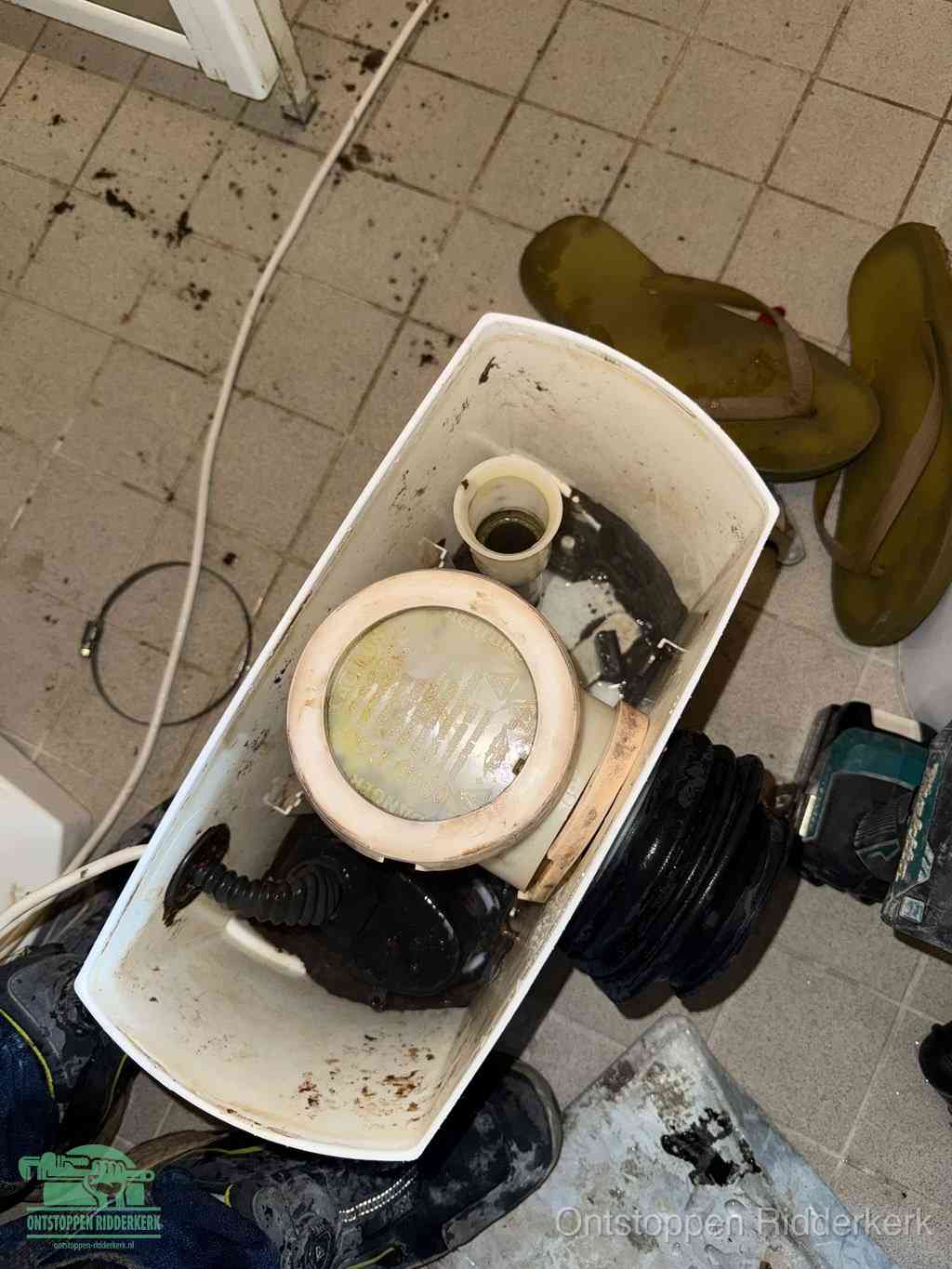 Een gedemonteerde toiletpot op de vloer met ontstoppingsveer en gereedschap ernaast, het verwijderen van een vastzittend voorwerp uit de wc in Ridderkerk