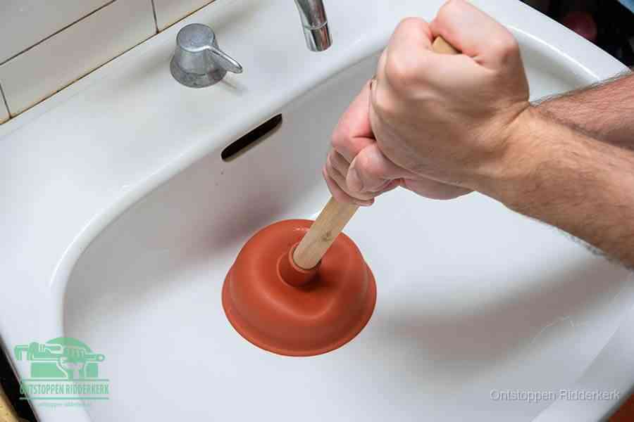 Twee handen gebruiken een rode rubberen plopper op een sanitair-afvoer om het toilet te ontstoppen in Ridderkerk