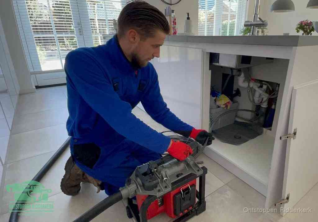 Een monteur voert een professionele elektrische ontstoppingsmachine in de afvoer onder de spoelbak tijdens het gootsteen ontstoppen in Ridderkerk