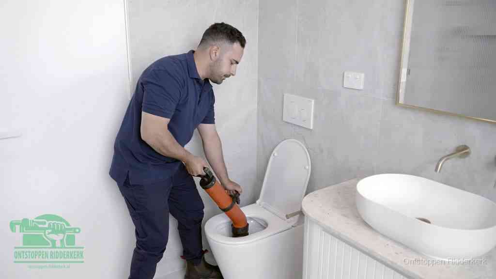 Een man gebruikt een handmatige luchtdruk-ontstopper in een modern betegeld toilet om zelf de wc te ontstoppen in Ridderkerk